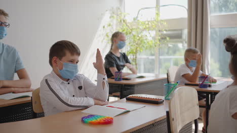 Raise-your-hand-to-answer-the-teacher's-question.-Multi-ethnic-group-of-children-with-face-masks-at-school-during-COVID-19-pandemic.